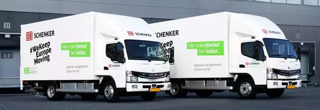 Two electric DB Schenker delivery trucks in front of a distribution center in Tilburg